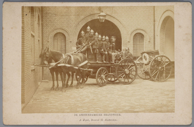 Oud brandweerlieden op een bluswagen van de Amsterdamsche Brandweer op de binnenplaats van de Hoofdwacht Prinsengracht